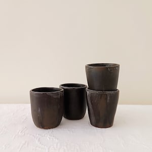 Könnte beinhalten: Vier braune Keramikbecher, die übereinander gestapelt sind. Die Becher sind alle gleich groß und haben die gleiche Form, und sie haben eine leicht strukturierte Oberfläche.