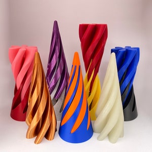 May include: A collection of seven colourful 3D printed cones, each with a unique spiral design. The cones are made of plastic and are available in a variety of colours, including red, orange, yellow, green, blue, purple, and pink.