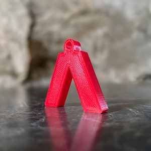 Puede incluir: Un colgante de plástico rojo brillante en forma de triángulo con un pequeño agujero en la parte superior.