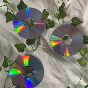 Könnte beinhalten: Drei silberne CDs mit schillernden Regenbogenreflexen auf weißem Hintergrund mit grünen Efeu-Ranken.
