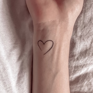 May include: A simple black heart drawn on a person's wrist.