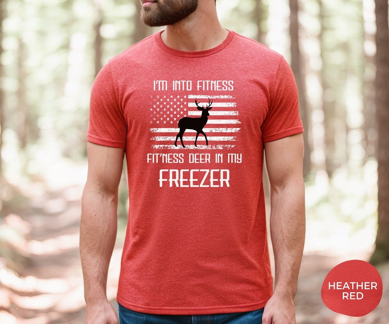 Puede incluir: Camiseta roja con una silueta de ciervo blanca y un gr&aacute;fico de bandera estadounidense. El texto dice "I'm into fitness fitness deer in my freezer".
