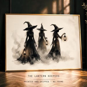 May include: A framed horizontal wall art print titled THE LANTERN KEEPERS featuring three silhouetted figures in long dark dresses and pointed hats, each carrying a glowing lantern amidst a soft, smoky, off-white background.
