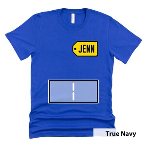 Puede incluir: Una camiseta azul real con una etiqueta amarilla que dice "JENN" y un rect&aacute;ngulo azul con dos l&iacute;neas blancas en el centro.