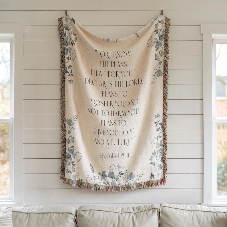 May include: Cream-colored woven throw blanket with a floral design in shades of blue and gray. The blanket features the text "FOR I KNOW THE PLANS I HAVE FOR YOU..." from Jeremiah 29:11. The edges have a fringed trim.