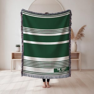 May include: Green and white striped throw blanket with fringe edges. The blanket has a rectangular label with the text "THE JONES EST. 2001". The blanket is made of a soft, woven material.