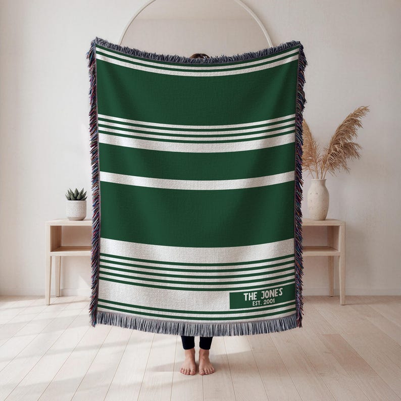 May include: Green and white striped throw blanket with fringe edges. The blanket has a rectangular label with the text "THE JONES EST. 2001". The blanket is made of a soft, woven material.
