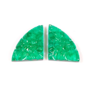 May include: Two carved green gemstone cabochons in the shape of half circles. The cabochons are carved with a floral design.