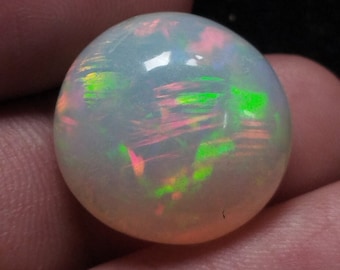 May include: A round, white opal gemstone with iridescent green, pink, and yellow flashes. The opal is smooth and polished.