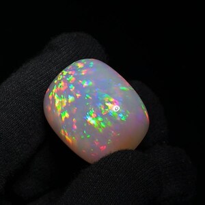 K&ouml;nnte beinhalten: Ein wei&szlig;er Opal-Cabochon mit einem Regenbogen aus irisierenden Farben. Der Opal ist ein nat&uuml;rlicher Edelstein mit einer glatten, polierten Oberfl&auml;che.