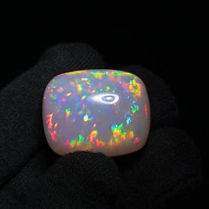 K&ouml;nnte beinhalten: Ein wei&szlig;er Opal-Cabochon mit einem Regenbogen aus Farben, darunter Rot, Orange, Gelb, Gr&uuml;n, Blau und Lila. Der Opal ist in einem Silberring gefasst.