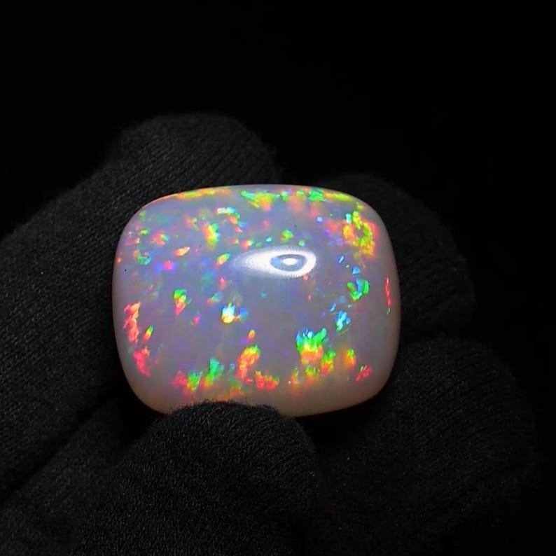 K&ouml;nnte beinhalten: Ein wei&szlig;er Opal-Cabochon mit einem Regenbogen aus Farben, darunter Rot, Orange, Gelb, Gr&uuml;n, Blau und Lila. Der Opal ist in einem Silberring gefasst.