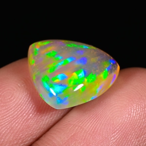 Könnte beinhalten: Ein dreieckiger, irisierender Opal-Edelstein mit einer weißen Basis und Blitzen von Grün, Blau und Orange.