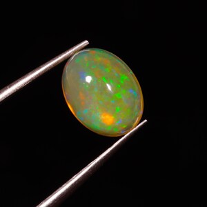 Könnte beinhalten: Ein ovaler Opal-Edelstein in Grün und Weiß mit schillernden Farbeffekten.