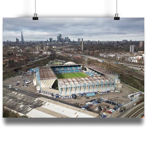 Peut inclure: Vue aérienne d'un grand stade de football bleu et blanc avec un terrain vert. Le stade est entouré d'un parking et d'une ville en arrière-plan.