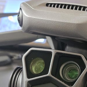 May include: A close-up of a black drone camera with three lenses. The camera has the Hasselblad logo on the front.