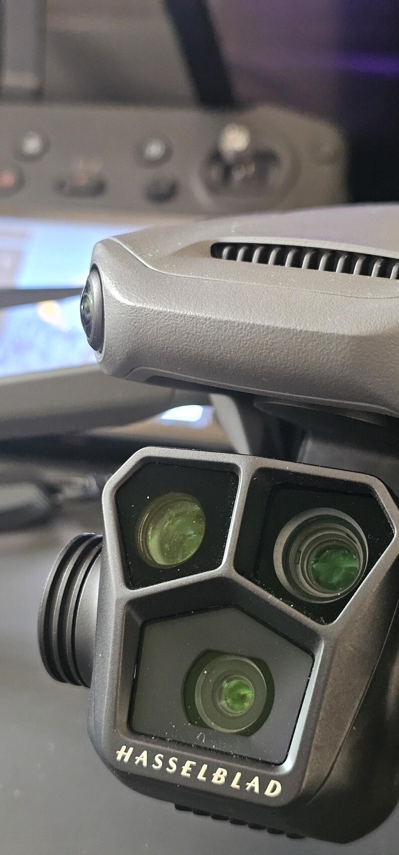 May include: A close-up of a black drone camera with three lenses. The camera has the Hasselblad logo on the front.