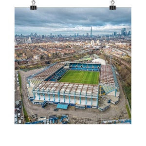 Peut inclure: Vue aérienne d'un grand stade de football bleu et blanc avec un terrain vert. Le stade est entouré d'un parking et d'une ville en arrière-plan.