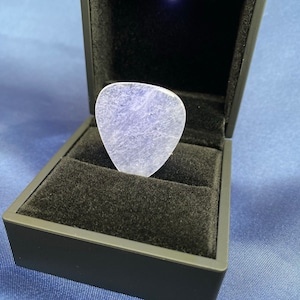 Może przedstawiać: Przezroczysty plektron gitarowy z tworzywa sztucznego w czarnym pudełku na pierścionek wyłożonym aksamitem.