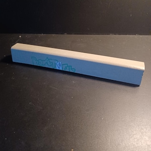 May include: A rectangular, light gray concrete fingerboard obstacle with a smooth, flat top surface. The side features a teal-colored graphic print with the text "BOOSTED" and a small circular icon containing a stylized skull design.
