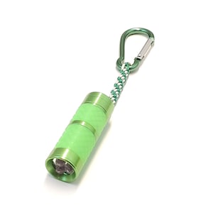May include: A lime green cylindrical flashlight with a textured grip and a metallic finish. The flashlight features a green carabiner attached by a braided white and green cord. Three small light bulbs are visible inside the front lens.