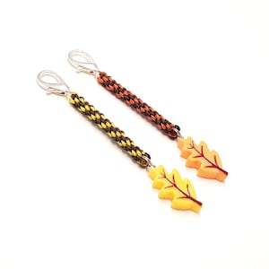 May include: Two zipper pulls featuring braided cords attached to silver-tone lobster clasps. One pull has a yellow oak leaf charm with brown veins, and the other has an orange oak leaf charm with brown veins and a dark brown and orange cord.