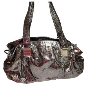 May include: Metallic silver handbag with a snakeskin pattern. The bag has two handles and a rectangular silver metal plate with the brand name. The bag is a tote style.