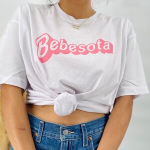 May include: White t-shirt with a pink graphic that says "Bebesota" in a retro font.
