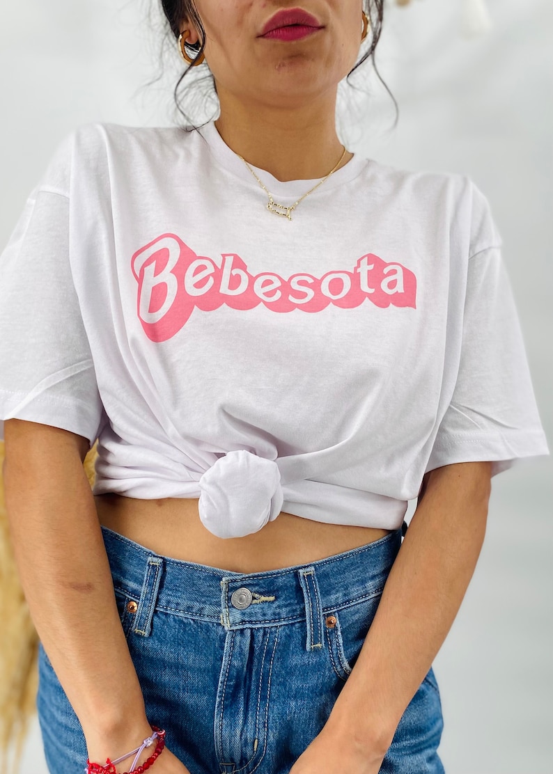 May include: White t-shirt with a pink graphic that says "Bebesota" in a retro font.