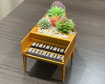 May include: A miniature wooden harpsichord with a white and brown keyboard, converted into a planter with a variety of green and pink succulents.