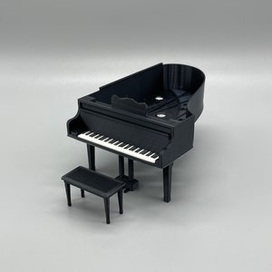 May include: A black grand piano with a white keyboard and a matching black piano bench. The piano is made of plastic and is a miniature model.