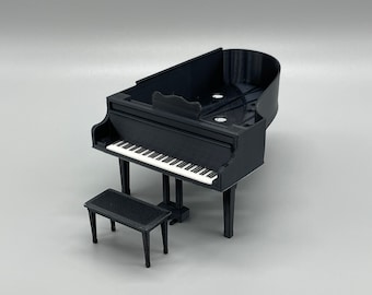 May include: A black grand piano with a white keyboard and a matching black piano bench. The piano is made of plastic and is a miniature model.