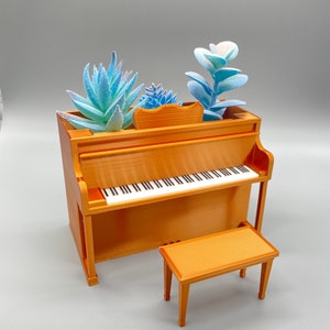 May include: A miniature gold-colored piano with a bench, decorated with blue and green artificial succulents.