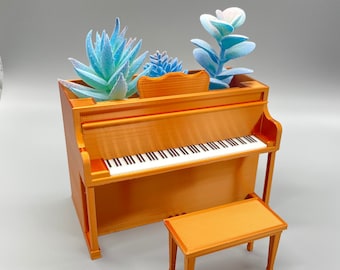 May include: A miniature gold-colored piano with a bench, decorated with blue and green artificial succulents.