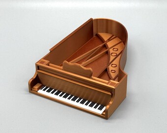 May include: A miniature wooden grand piano model in a brown finish. The piano has a white keyboard and a detailed interior.