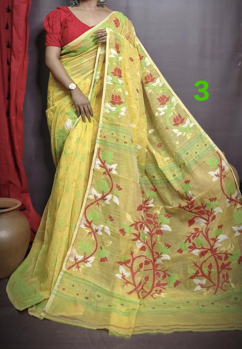 May include: A yellow saree with a floral pattern in red, green, and white. The saree has a thin border with a repeating pattern.