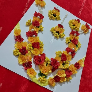 May include: A set of red and yellow flower jewellery for a bride or bridesmaid. The set includes a necklace, earrings, and a maang tikka.