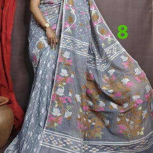 May include: A gray and white saree with a floral pattern. The saree has a pink and gold border. The saree is draped over a person's body. The number 8 is visible in the upper right corner of the image.