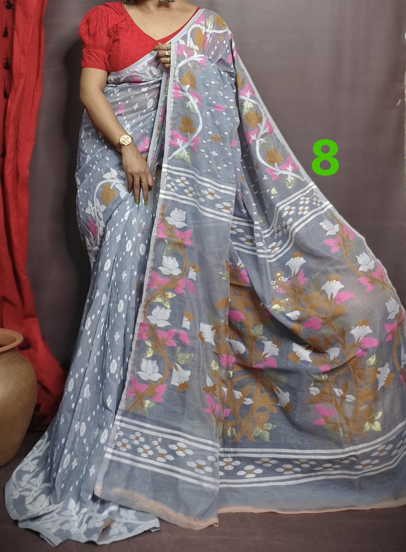 May include: A gray and white saree with a floral pattern. The saree has a pink and gold border. The saree is draped over a person's body. The number 8 is visible in the upper right corner of the image.