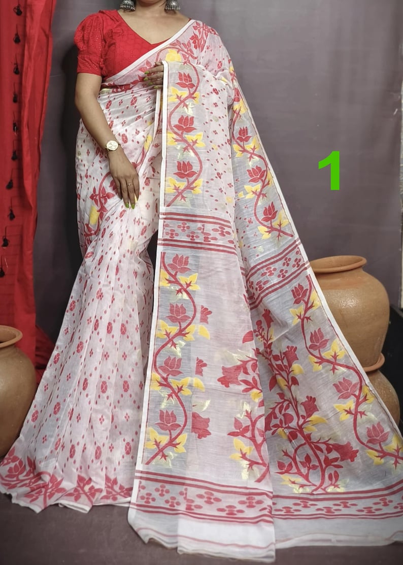 May include: White saree with red and yellow floral patterns. The saree has a thin, transparent fabric with a delicate design. The saree is draped over a person's body, and the fabric is flowing.