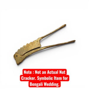 May include: A brass-colored, decorative nutcracker with a unique, stylized design. The tool features a serrated edge and long, slender handles. Text on the image reads: "Note: Not an Actual Nut Cracker. Symbolic Item for Bengali Wedding."