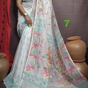 May include: White saree with a floral pattern in pink, blue, and gold. The saree has a thin gold border and a light blue and white striped border.