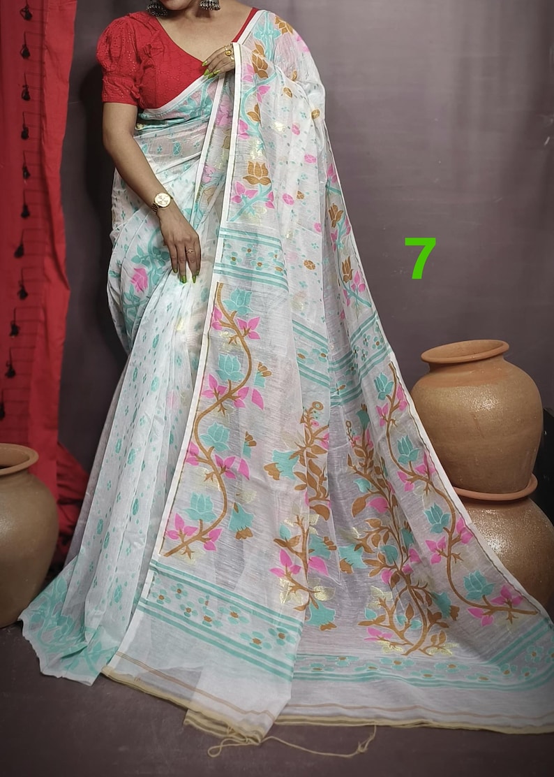 May include: White saree with a floral pattern in pink, blue, and gold. The saree has a thin gold border and a light blue and white striped border.