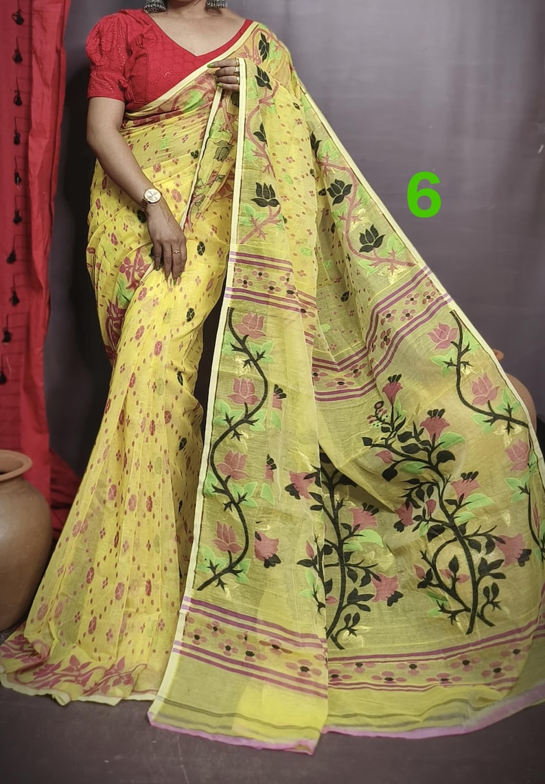 May include: A yellow saree with a floral pattern and a red border. The saree is made of a lightweight fabric and has a delicate, feminine feel.