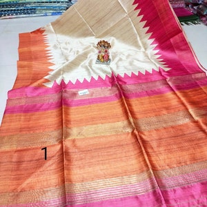 May include: A vibrant saree with a cream-colored center and a striking pink and orange border. The design features a zigzag pattern along the edges and horizontal stripes. A small figurine sits on the saree.