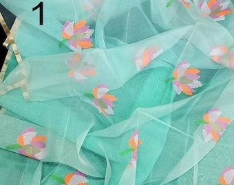 May include: A sheer turquoise fabric with embroidered floral designs in shades of pink, orange, and white. The fabric has a subtle striped pattern along the edges.