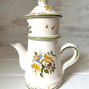 Peut inclure: Une cafetière en céramique blanche avec un motif floral vert et jaune. La cafetière a un couvercle et un bec verseur. C'est une cafetière de style vintage.