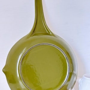 May include: The underside of a green cast iron frying pan with a long handle. The pan has a smooth, glossy finish.
