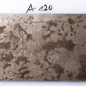 May include: A close-up of a metallic surface with a textured, marbled pattern in shades of brown and silver. The surface has a worn, aged appearance, with visible scratches and imperfections. The text "A 120" is written in black ink in the top right corner.
