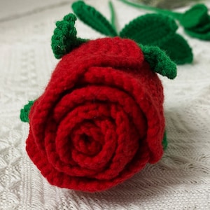 May include: A red crocheted rose with green crocheted leaves. The rose is made of yarn and is a handmade craft.